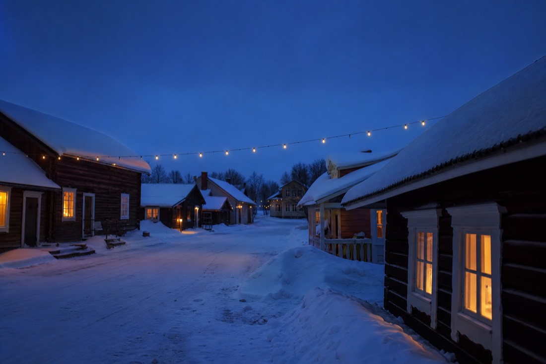 A snowy Nordic village street at dusk with warm lit windows in Finnish Lapland