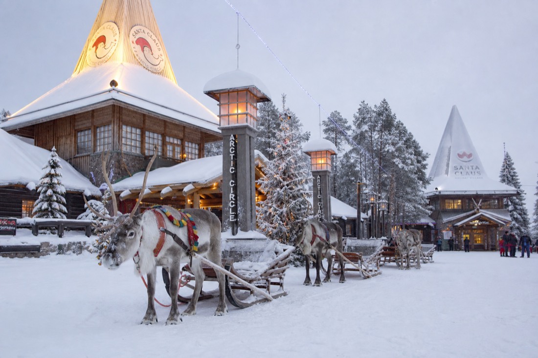 Villaggio di Babbo Natale a Rovaniemi con renne all'esterno di edifici in legno, finestre illuminate, paesaggio artico innevato
