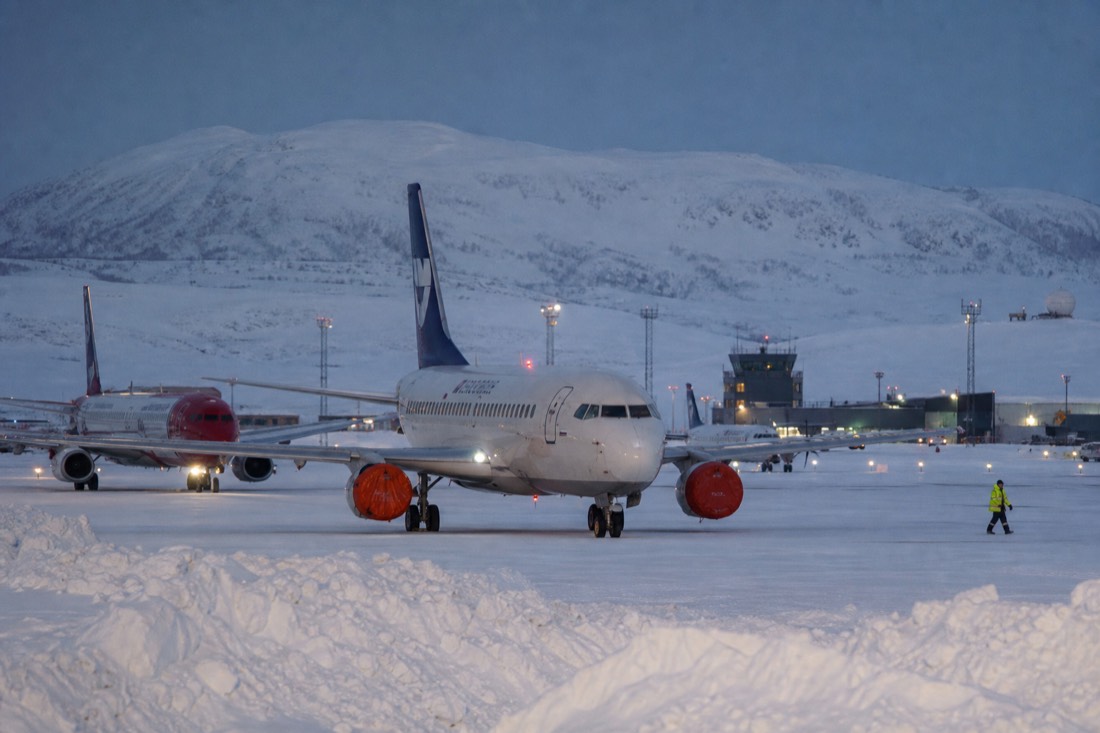 A small regional airport apron in deep Arctic snow, runway lights glowing, snowbanks, aircraft waiting