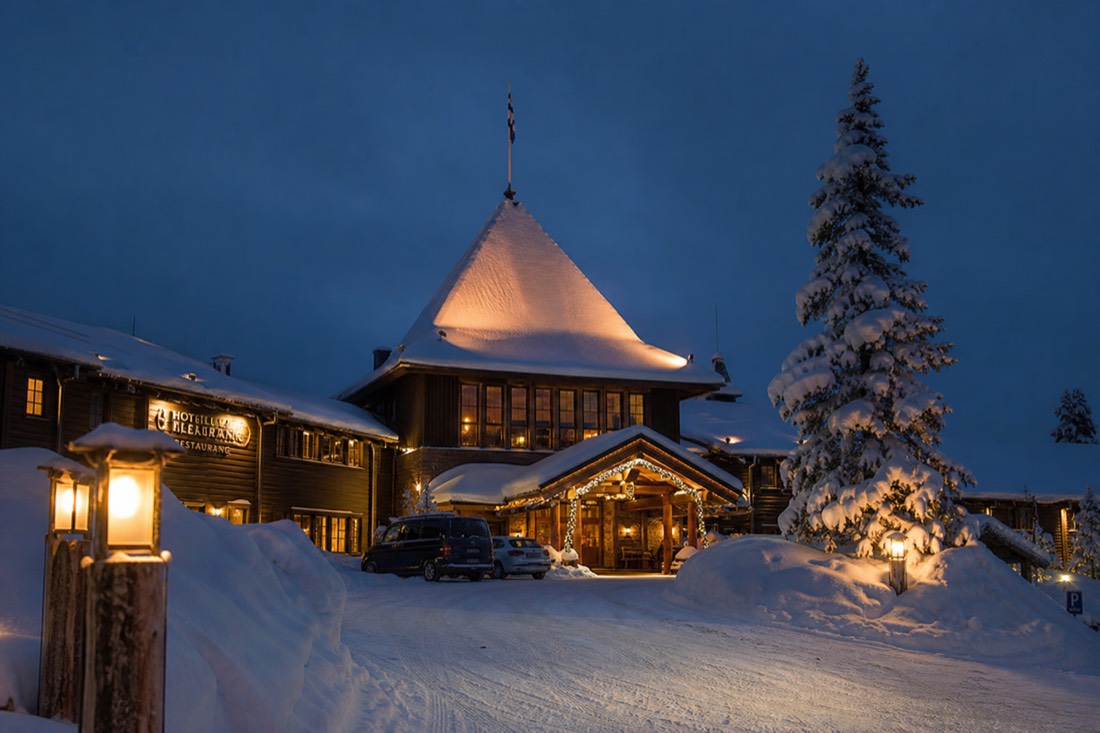 A luxury Lapland hotel exterior in deep snow at twilight, warm glowing windows, wooden Nordic architecture