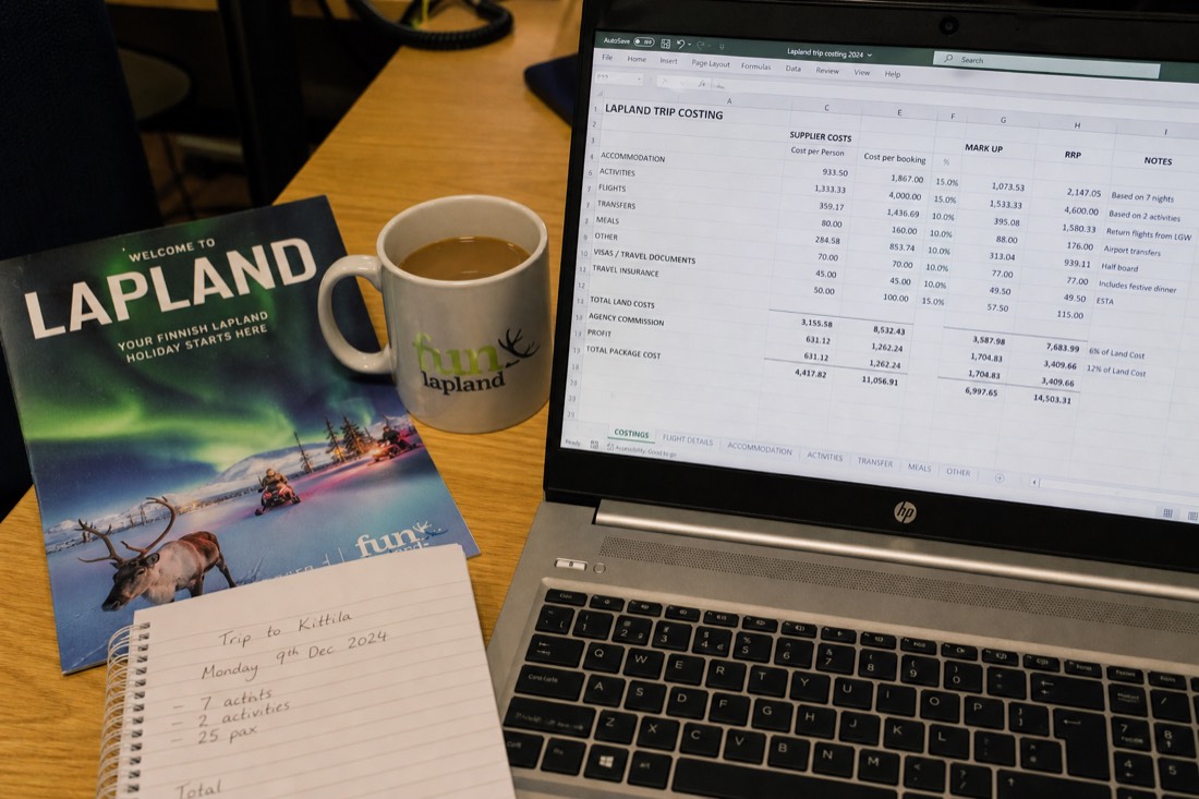 A spreadsheet with travel costs and pricing data on a desk with Lapland travel brochures and a coffee cup