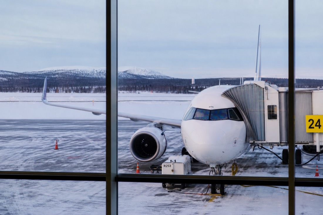 Modern commercial aircraft parked at a Lapland airport gate with snow-covered tarmac and Nordic landscape beyond windows