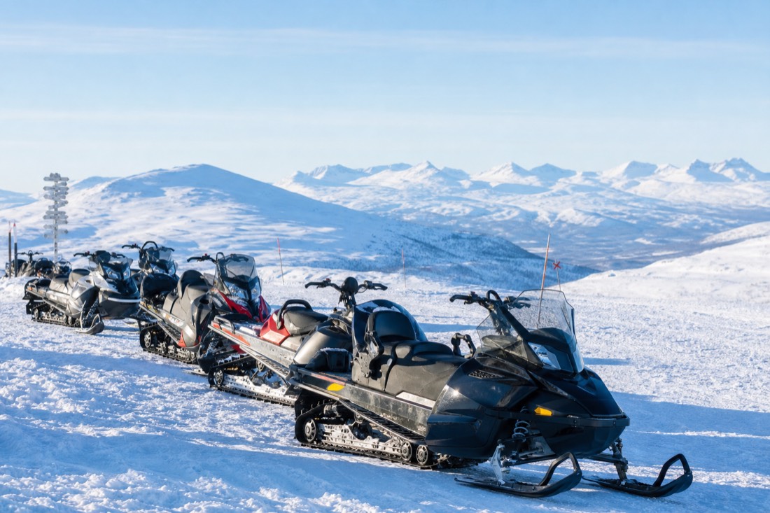 A group of modern snowmobiles parked in formation on deep snow, mountains visible in distance, Lapland winter landscape